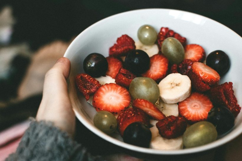 A close-up of a bowl filled with fresh strawberries, grapes, banana slices, and raspberries.